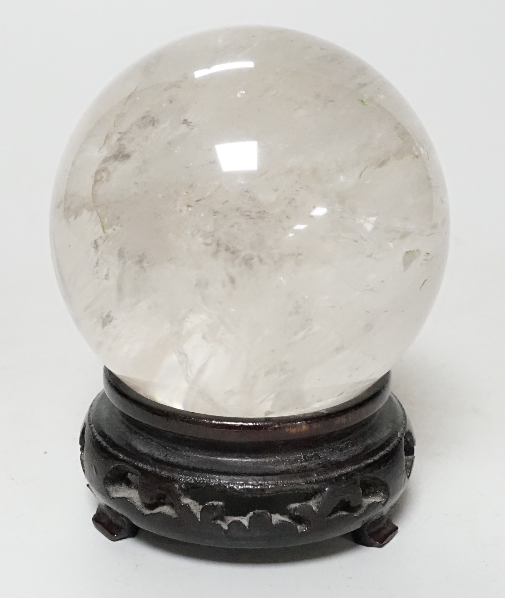 A rock crystal quartz sphere, probably from Brazil, on a carved wood stand, 10cm tall